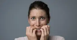 Przerażona kobieta gryzie paznokcie, jej oczy szeroko otwarte. Wygląda, jakby zmagała się z fobią przed dziurami, widząc je wszędzie.