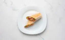 Kebab w tortilli z kurczakiem, pokrojony na pół, na białym talerzu.