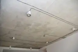 Nowoczesna instalacja elektryczna natynkowa na betonowym suficie z kilkoma białymi oprawami oświetleniowymi.