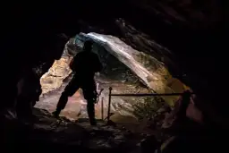 Sylwetka człowieka w jaskini wielkiej śnieżnej, oświetlonej od środka. Skały i stalaktyty tworzą mroczny, tajemniczy krajobraz.