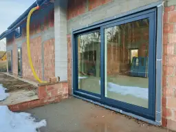 Nowe okna przesuwne w trakcie ciepłego montażu. Widać izolację i przygotowanie do wykończenia.