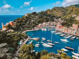 Malowniczy widok na zatokę z kolorowymi domami i licznymi łodziami. Tak właśnie wygląda Portofino, gdzie leży ten urokliwy włoski kurort.