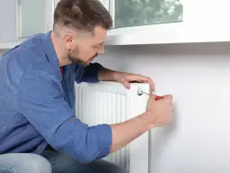 Mężczyzna odpowietrza kaloryfer w bloku, używając śrubokręta.