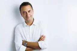 Mężczyzna w białej koszuli, z rękami skrzyżowanymi na piersi, prezentuje pewne siebie pozy do zdjęć męskie. Uśmiecha się lekko do obiektywu.