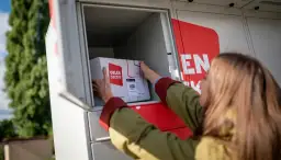 Kobieta wkłada paczkę z logo "Orlen paczka" do skrytki automatu paczkowego.