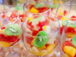 Kilka kieliszków z galaretką owocową, w tym kiwi, truskawkami i brzoskwiniami.
