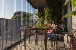 Jak zrobić balkon w bloku? Przytulny, przeszklony balkon ze stolikiem, krzesłami i mnóstwem zieleni. Idealne miejsce na poranną kawę.