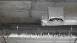 Izolowane rury wentylacyjne z okrągłym nawiewnikiem pod betonowym sufitem.