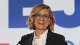 Kobieta w okularach i ciemnej marynarce śmieje się, stojąc przy mównicy.