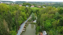 Widok z lotu ptaka na łowisko pstrągowe otoczone zielonymi drzewami, z domami w tle.