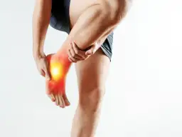 Mężczyzna trzymający się za bolącą stopę z zaznaczonym bólem.