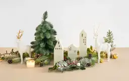 Bożonarodzeniowa dekoracja: białe renifery, choinka, ceramiczne domki, lampki i szyszki.