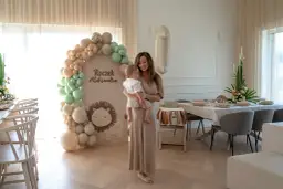 Elegancka sukienka i sandałki to idealny wybór, jak się ubrać na roczek jako gość. W tle dekoracje z balonów i lew.