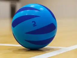 Niebieska piłka do pilatesu z ciemniejszymi pasami na drewnianej podłodze.