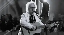 Zegarmistrz światła purpurowy chwyty na gitarze, w białej marynarce, śpiewa do mikrofonu.