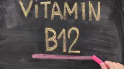 Kreidezeichnung "VITAMIN B12" auf einer Tafel, daneben eine Hand mit pinker Kreide.