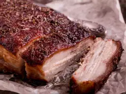 Soczysty, chrupiący boczek pieczony w piekarniku, posypany ziołami.