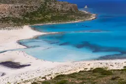 Widok na turkusową zatokę z piaszczystą plażą i skalistym wybrzeżem.