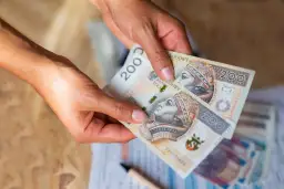 Dłonie trzymają banknoty 200 zł. Czy na lokatę można wpłacać pieniądze co miesiąc?