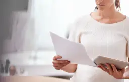 Kobieta analizuje dokumenty, zastanawiając się, czy można przełożyć sprawę w sądzie.