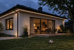 Elewacja domu oświetlona ciepłym światłem LED od dołu, tworząc przytulną atmosferę. Piłka na trawniku sugeruje wieczorne zabawy.