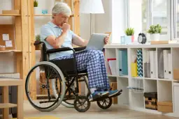 Starszy mężczyzna na wózku inwalidzkim zamyślony nad laptopem, jakby zastanawiał się, jaki lekarz wypełnia wniosek o niepełnosprawność.