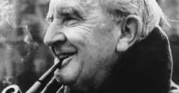 J.R.R. Tolkien, autor książki Hobbit, pali fajkę, uśmiechając się.