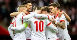 Piłkarze reprezentacji Polski w białych strojach świętują razem, przytulając się.