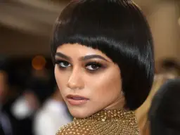 Krótka, błyszcząca paź fryzura podkreśla spojrzenie kobiety z mocnym makijażem oczu.