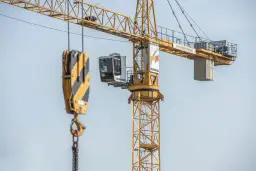 Żółty dźwig budowlany z kabiną operatora i hakiem. Widać fragmenty konstrukcji i logo Liebherr.