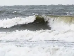 Potężne fale rozbijają się o brzeg, pokazując siłę, kiedy są sztormy na Bałtyku. Woda jest wzburzona i szara.