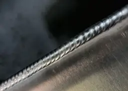 Precyzyjne spawanie na zimno metalowych elementów, widoczna struktura spoiny.