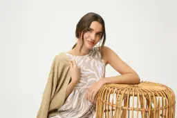 Eleganckie stylizacje na urodziny w lokalu: młoda kobieta w beżowej sukience w panterkę i kardiganie, oparta o wiklinowy stołek.