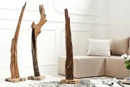 Drei skulpturale Treibhölzer auf Holzsockeln in einem hellen Raum mit Sofa und Kissen.