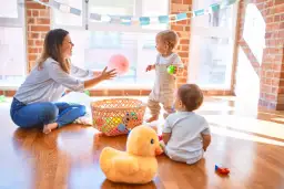 Mama bawi się z dziećmi, rzucając różową piłeczką. Wesołe gry logopedyczne dla 4 latka, pełne kolorowych zabawek w koszyku.