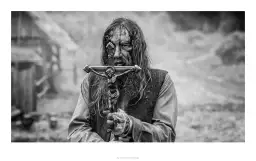 Mroczna recenzja książki "Malowany ptak". Postać z krucyfiksem, w brudnych ubraniach, z zakrwawioną twarzą.