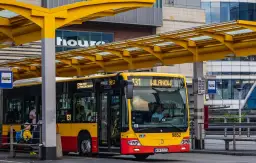 Żółto-czerwony autobus miejski na przystanku. Kierowca autobusu PKS, jak i jego zarobki, to temat dyskusji, ale ten pojazd wozi pasażerów.