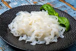 Makaron konjac na czarnym talerzu, z listkiem bazylii. To zdrowa alternatywa dla tradycyjnych klusek.