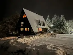 Drewniany domek oświetlony ciepłym światłem, otoczony śniegiem i choinkami. Idealne miejsce na zimowy wypoczynek na przełęczy okraj.