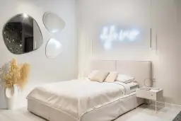 Nowoczesne oświetlenie sypialni inspiracje: neonowy napis, wiszące lampy i lustra o organicznych kształtach tworzą przytulną atmosferę.