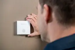 Mężczyzna sprawdza czujnik czadu Honeywell Home. Pamiętaj, czujnik czadu co ile wymieniać, by zapewnić bezpieczeństwo.