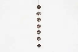 Wisząca ozdoba z siedmioma symbolami czakr na białej, teksturowanej ścianie.