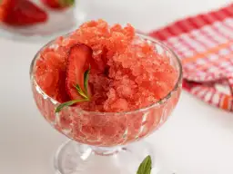 Sorbet truskawkowy w pucharku, ozdobiony plasterkiem truskawki i miętą.