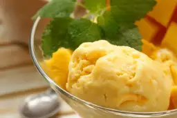Domowe lody mango z miętą w szklanej miseczce.