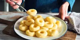 Talerz pełen gotowanych klusek śląskich, jedna kluska na łyżce.