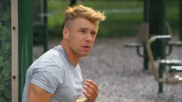 Młody mężczyzna z blond włosami, w szarej koszulce, siedzi na siłowni plenerowej. Czy Skolim gra jeszcze w barwach szczęścia?