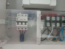 Trzybiegunowy wyłącznik nadprądowy w obudowie z przezroczystego plastiku, podłączony do przewodów.