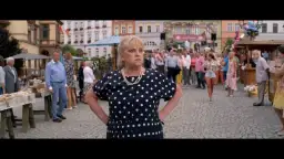 Kobieta w grochy na targu, gdzie kręcono miłość jest blisko. W tle tłum ludzi i kolorowe kamienice.