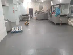 Nowa, szara wylewka betonowa w kuchni przemysłowej schnie, czekając na dalsze prace.