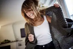 Uśmiechnięta młoda kobieta w swetrze, jakby szukała odpowiedzi na pytanie "co to jest szczęście cytaty".